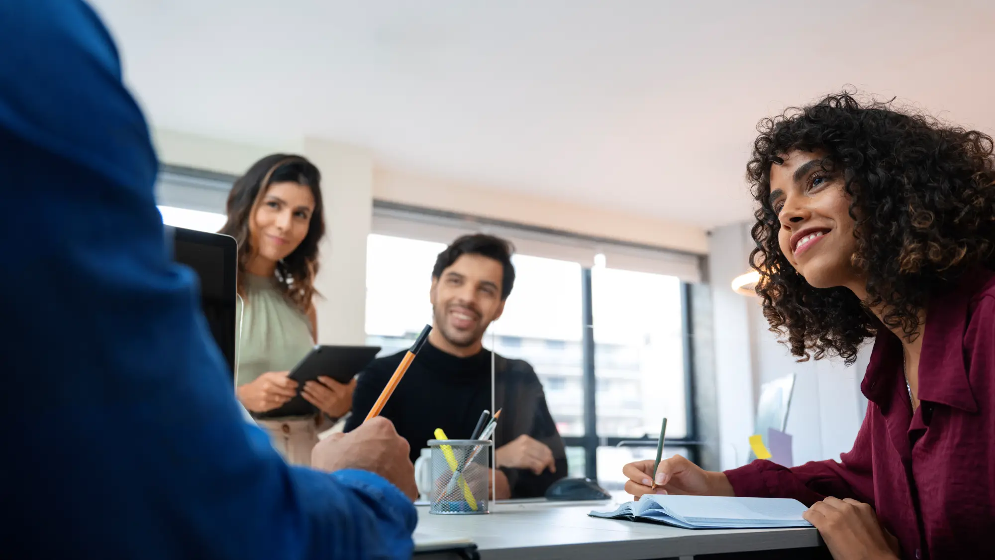 Profissionais sorrindo durante uma reunião colaborativa em um escritório iluminado.
