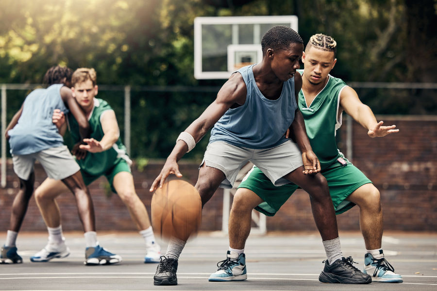 Quatro adolescentes jogando uma partida de basquete.