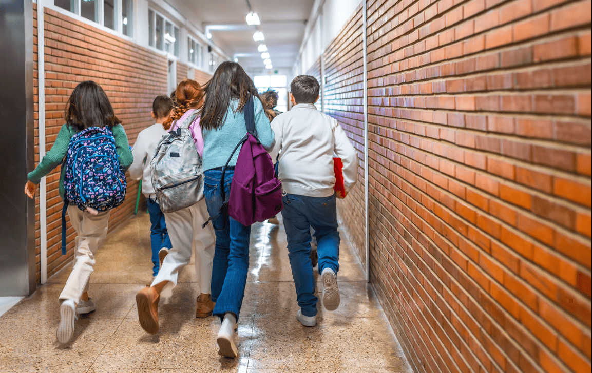 Estudante de costas com mochila caminhando pelo corredor de uma escola.